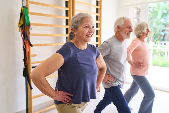 Senior Adults Exercising in Rehabilitation Center Lunges and Physical Therapy for Recovery and Wellness Indoor Gym Setting With Equipment