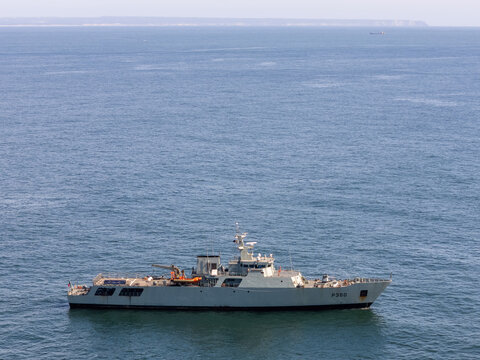 Aerial view of a grey naval patrol vessel P360 navigating the calm blue waters of the Atlantic Ocean off the coast of Cascais, Portugal.
