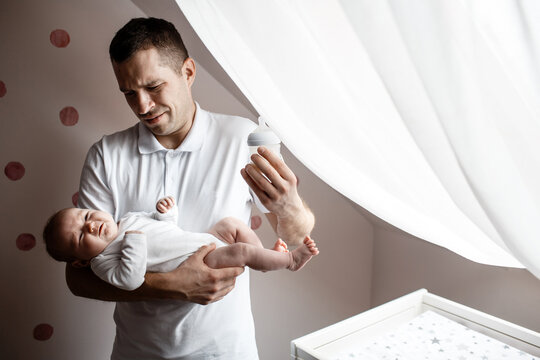 Father and little kid in the nursery. The first year of life. Uncertainty and fear of a child. Daddy does not know what to do with the child