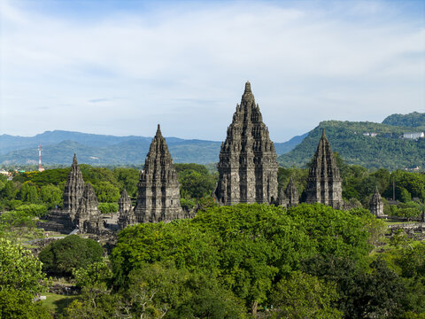 Aerial view of Prambanan Temple with its ancient stone towers rising above lush tropical trees and mountains in the background Prambanan, Daerah Istimewa Yogyakarta, Indonesia.
