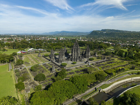 Aerial view of the ancient Prambanan Temple complex featuring towering stone spires and lush green grounds under a bright blue sky in Prambanan, Daerah Istimewa Yogya, Indonesia.