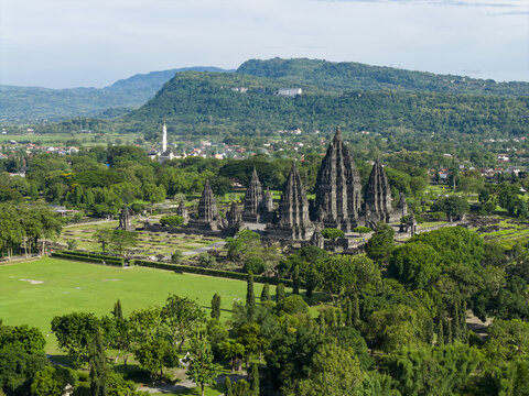 Aerial view of the ancient Prambanan Temple complex with its towering stone structures surrounded by lush green lawns and distant hills in Prambanan, Daerah Istimewa Yogya, Indonesia.