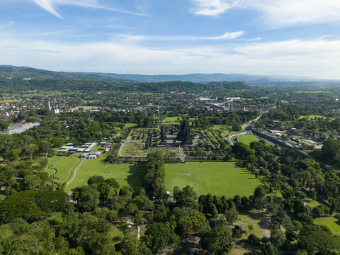 Aerial view of the ancient Prambanan Temple complex with its towering stone spires surrounded by lush green lawns and the urban landscape of Prambanan, Daerah Istimewa Yogya, Indonesia.