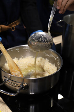 chef cocinando arroz en una olla echando caldo al guiso con cazo