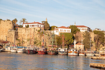 Naklejka premium Historic harbor of Kaleiçi old town with moored boats and ancient city walls at sunset