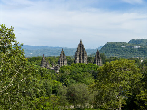 Aerial view of Prambanan Temple, the ancient Hindu temple complex surrounded by lush tropical trees and distant mountains under a clear sky Prambanan, Daerah Istimewa Yogya, Indonesia.
