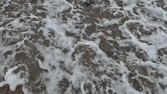 Heart sand wave drawing on beach is washed away by foamy sea water representing the concept of transient love and fleeting memories