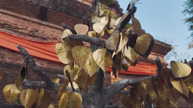 Golden leaf tree with engraved wishes at Buddhist temple in Thailand, Sacred offering tree with metal leaves and prayers in Thai temple courtyard 4k