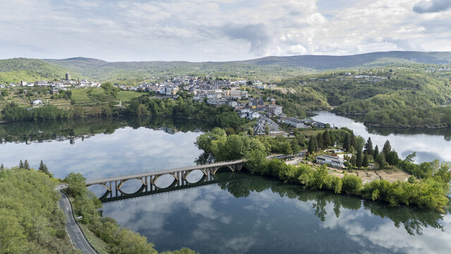 Aerial view of the town of Viana do Bolo situated on a peninsula with an arched bridge crossing the calm water reflecting the sky and surrounding green hills Viana do Bolo, Province of Ourense, Spain.