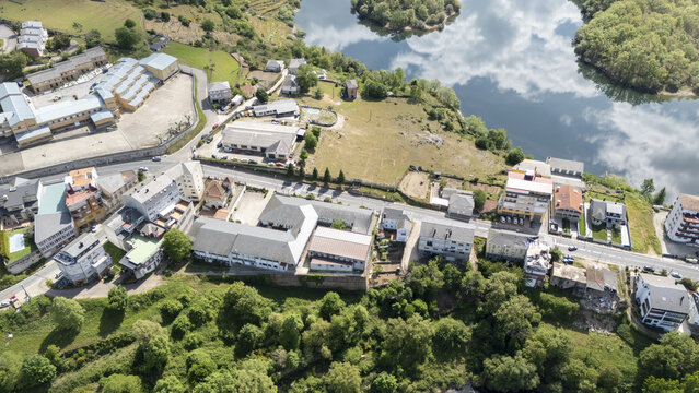 Aerial view of the town buildings and lush green hills overlooking the Bibei river reservoir with clouds reflecting in the water in Viana do Bolo, Province of Ourense, Spain.