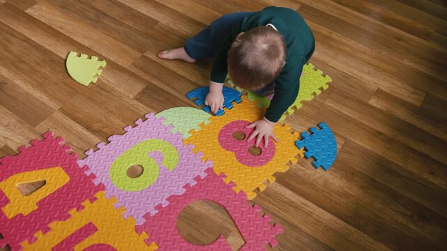 Little boy assembling a colorful foam number puzzle mat on the floor