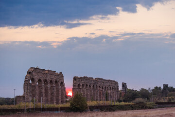 Fototapeta premium Sunset behind ancient Roman aqueduct in Parco degli Acquedotti Rome with warm light passing through arches and expansive evening sky