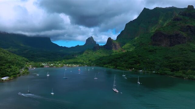 Tropical South Pacific Island Moorea, Bora Bora, French Polynesia, aerial drone view, Opunohu Bay Public Beach bright turquoise lagoons cruise power boat sailboat tall lush peaks Mount Rotui backwards