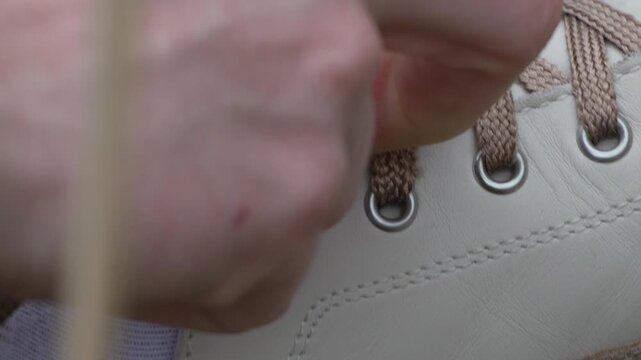 Shoelaces sneaker tying close up view of hands fastening brown laces on white leather shoes in preparation for a walk outdoors