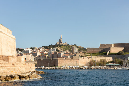 Vue sur la basilique Notre Dame de la Garde de Marseille depuis l'entr&eacute;e du Vieux Port, mer au premier plan, remparts du fort Saint Jean &agrave; gauche et citadelle &agrave; droite