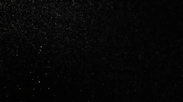 Abstract dark background with numerous small, bright, scattered particles creating a textured, grainy effect.