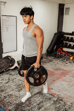 Handsome young Asian man does farmers walk at the gym to build grip strength and improve core stability with weighted plates