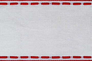 Craft project shows white fabric with red stitches in a simple border at a crafting table during daylight © Fleuronica
