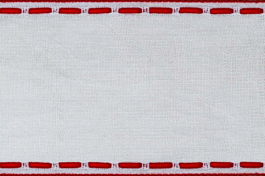 Craft project shows white fabric with red stitches in a simple border at a crafting table during daylight