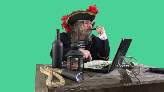 Elderly pirate types on a laptop with one finger, pipe in mouth, then recoils in comic fright at the screen. Old-world costume meets modern technology on a green screen