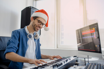 Merry Christmas and a happy new year! Composer hands on piano keys in recording studio. music production technology, man in christmas hat is working on pianino and computer keyboard on desk. © Vlad
