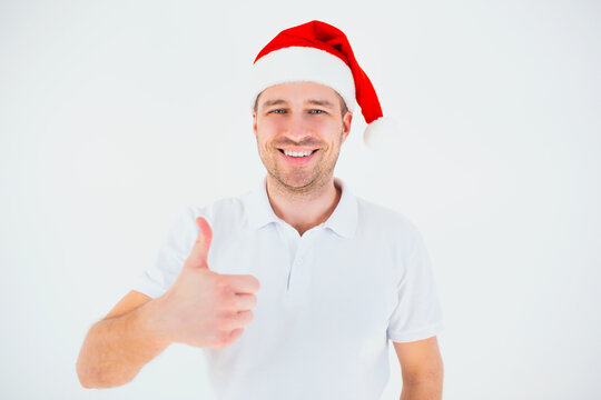 Young man isolated over white background. Guy in festive christmas red hat show big thumb up and smile. Cheerful positive nice guy posing on camera. Christmas time or new year period.
