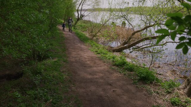 Father and little boy jogging together in a spring park near a river in slow motion