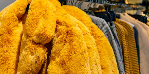 Furry yellow coats hang on a rack inside a clothing store in a busy shopping district during the winter season © Fleuronica