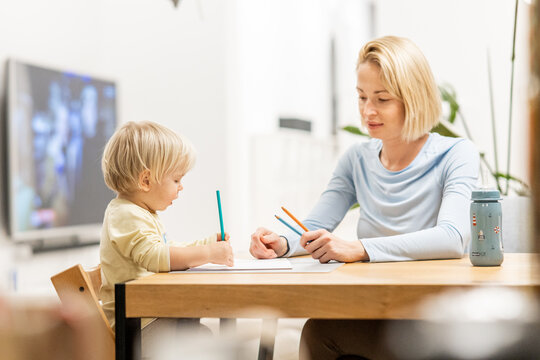 Caring young Caucasian mother and small son drawing painting in notebook at home together. Loving mom or nanny having fun learning and playing with her little 1,5 year old infant baby boy child