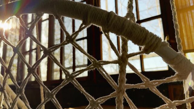 A textured woven macrame net hangs peacefully in a sun-drenched room. The glowing sunlight filters through the window, creating a calm, nostalgic, and deeply relaxing atmosphere.