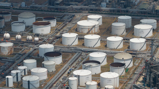 Aerial view of Bangchak Sriracha Refinery featuring large white oil storage tanks and industrial pipelines under bright daylight in Si Racha District, Chon Buri, Thailand.