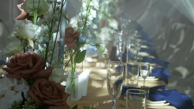 A close-up of a decorated table with glasses, plates and flowers in a restaurant at a banquet. A decorated table for a wedding celebration illuminated by spotlights.