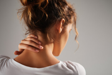 Obraz premium Aching Neck: A woman, captured from the rear, grips her neck, suggesting discomfort or pain. This image evokes feelings of tension and vulnerability.