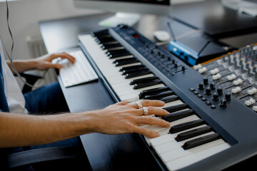 composer hands on piano keys in recording studio. music production technology, man is working on pianino and computer keyboard on desk. close up concept. © Vlad