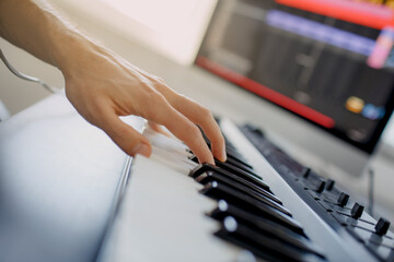 composer hands on piano keys in recording studio. music production technology, man is working on pianino and computer keyboard on desk. close up concept. © Vlad
