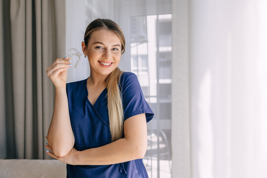 Smiling woman in professional attire holding an orthodontic transparent aligner