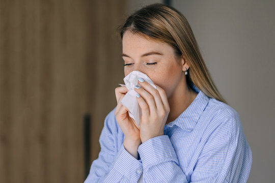 Young woman sneezing into a tissue, showing cold or allergy symptoms