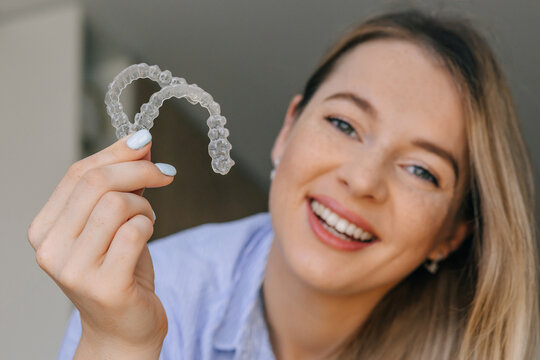 Smiling woman holding clear dental aligners for teeth straightening