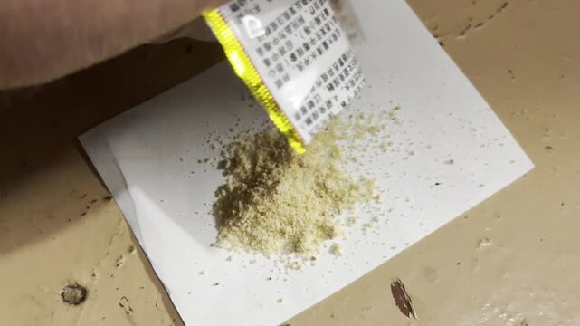A person shakes out yellow insect bait granules onto a white paper. This simple preparation gives a comforting feeling of cleanliness and careful control over the home.