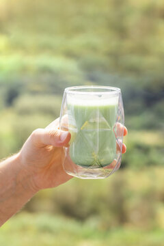 Hand Holding Glass of Refreshing Matcha Green Tea Outdoors