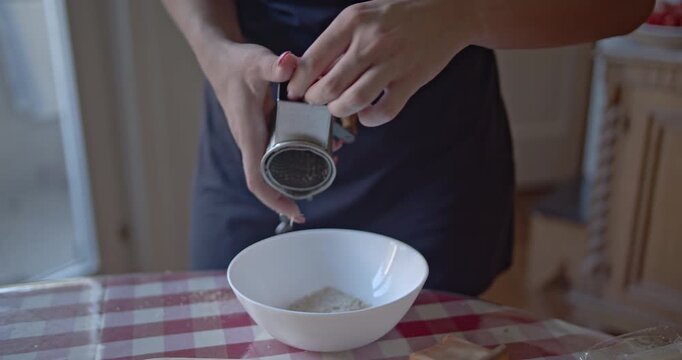 Close-up of a persons hands diligently preparing ingredients by grating stale bread into fine breadcrumbs. This culinary process takes place in a cozy home kitchen.