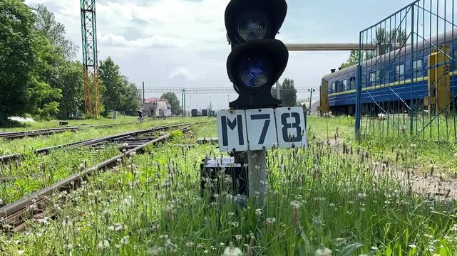 Low angle horizontal footage of railway signal, grassy tracks and passenger railcars at sunny train station with cinematic industrial atmosphere