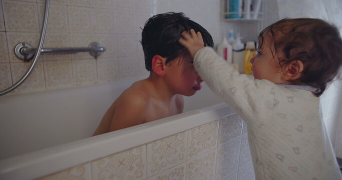 Baby toddler leaning to kiss older brother in bathtub during bath time showing playful affection sibling bond and tender family love indoors at home