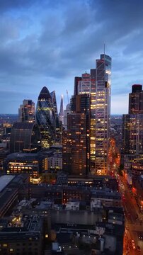 Establishing aerial view of the illuminated skyline at the City of London, UK, during dusk with street traffic