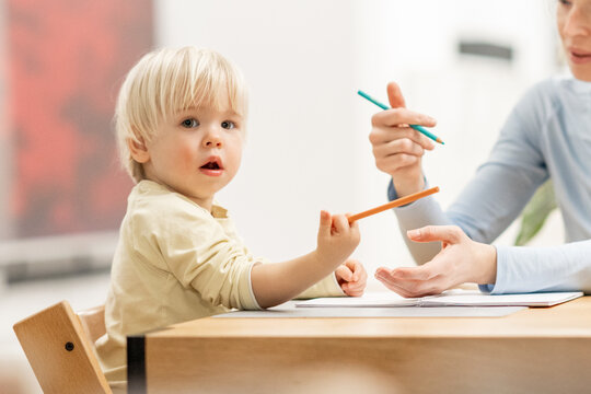 Caring young Caucasian mother and small son drawing painting in notebook at home together. Loving mom or nanny having fun learning and playing with her little 1,5 year old infant baby boy child