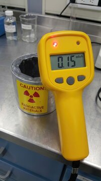 Radiation detector measuring dangerous dose, yellow instrument showing millisievert hour, scientific apparatus near radioactive container, laboratory equipment ensuring safety.