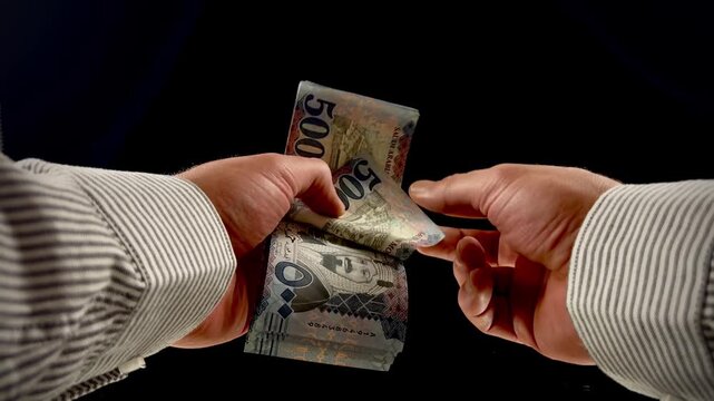 Hands counting Saudi Arabian Riyal banknotes on black background