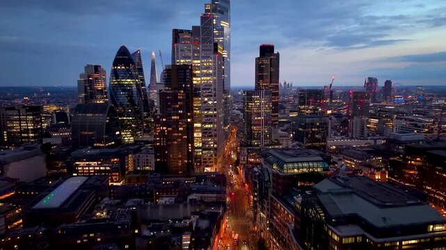Establishing aerial view of the illuminated skyline at the City of London, UK, during a moody evening with cloudscape