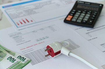 Fototapeta premium Documents show electricity bills with a calculator and cash on the table in a home office environment.
