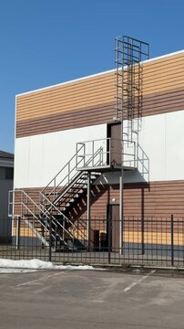 Modern building exterior with iron staircase, siding covered roof and metal ladder cage. Brown cladding over white wall